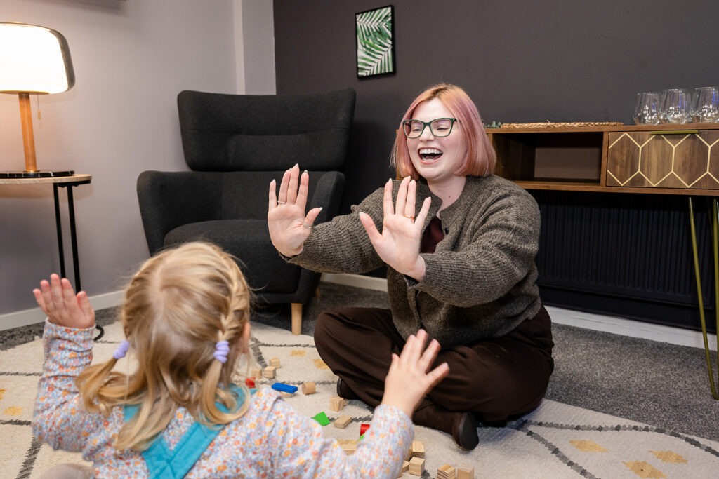 Charlotte sitting on the floor with a child clapping hands